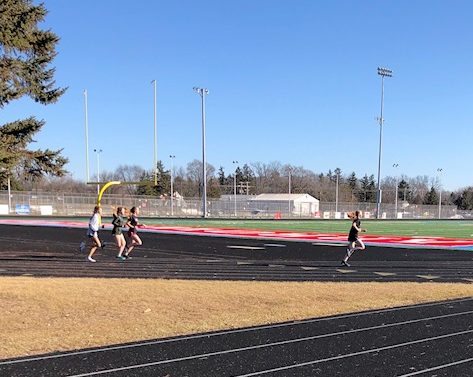 Girls track and field athletes run a warm up lap on the track before their sprints workout.